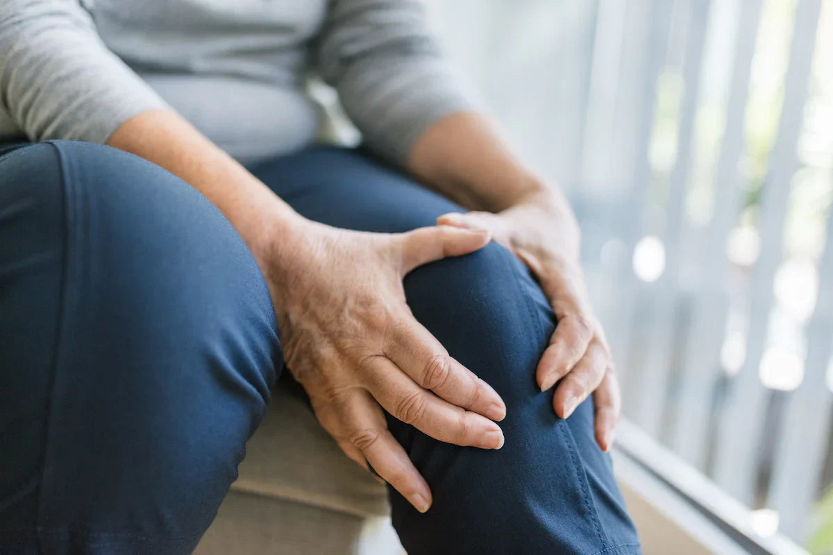Ältere Frau hält sich das schmerzende Knie – Symbol für Gelenkbeschwerden und eingeschränkte Beweglichkeit.