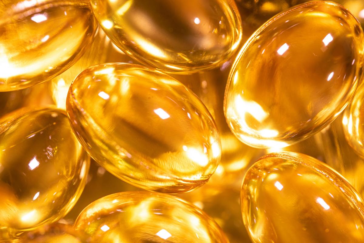 Nahaufnahme von goldfarbenen Omega-3-Kapseln mit glänzender Oberfläche und Lichtreflexionen.