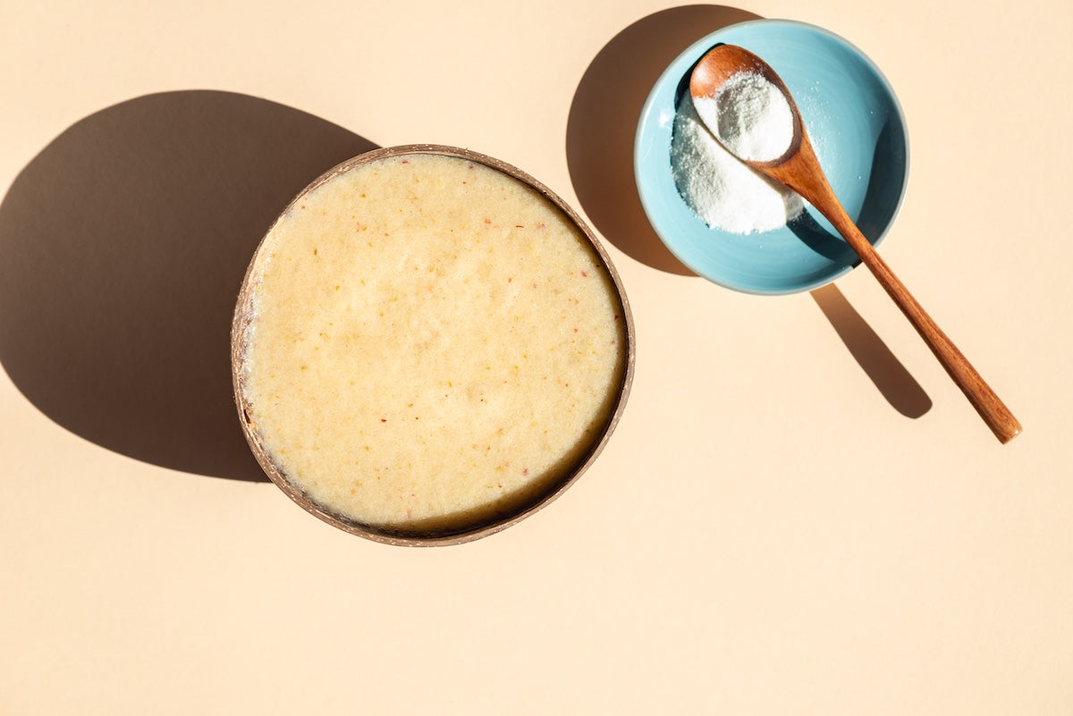 Schüssel mit cremigem Smoothie neben einer kleinen Schale mit weißem Kollagenpulver und Holzlöffel – Symbol für moderne Nahrungsergänzung.