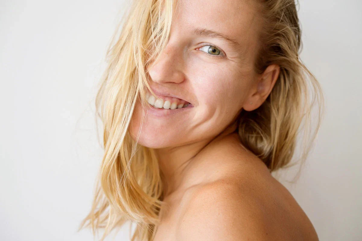 Nahaufnahme einer jungen Frau mit heller Haut und blonden Haaren, die ungeschminkt lächelt – Symbol für gesunde, strahlende Haut dank natürlichem Kollagen.