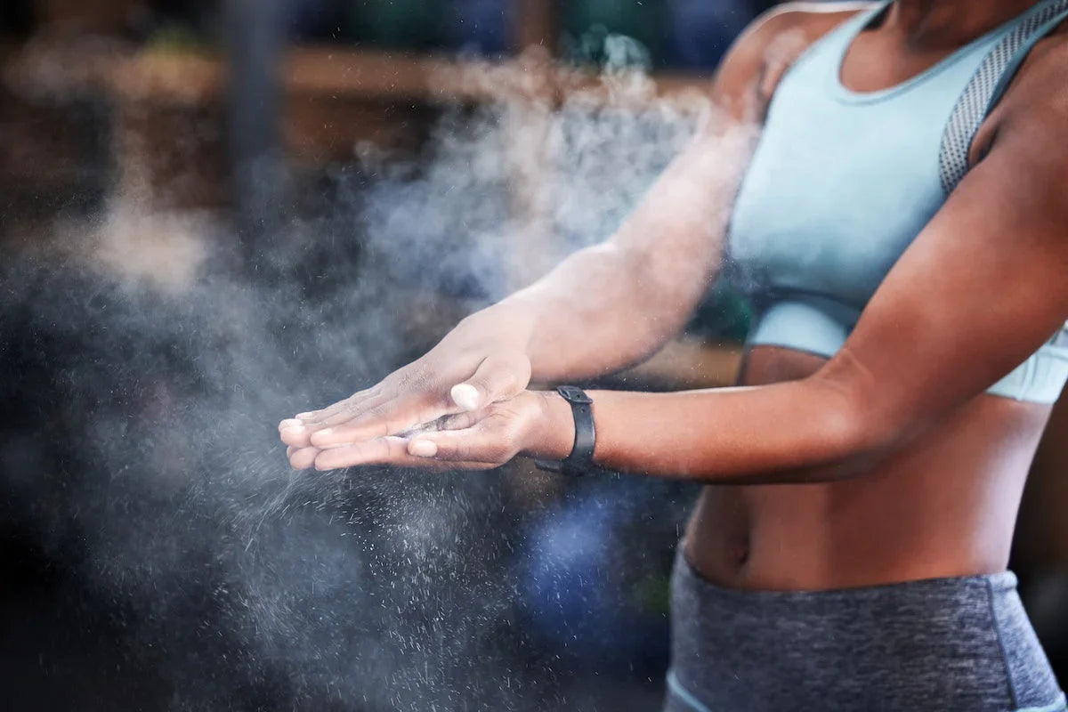 Sportliche Frau in einem Fitnessstudio klatscht die Hände zusammen, während sich Kreidestaub in der Luft verteilt.