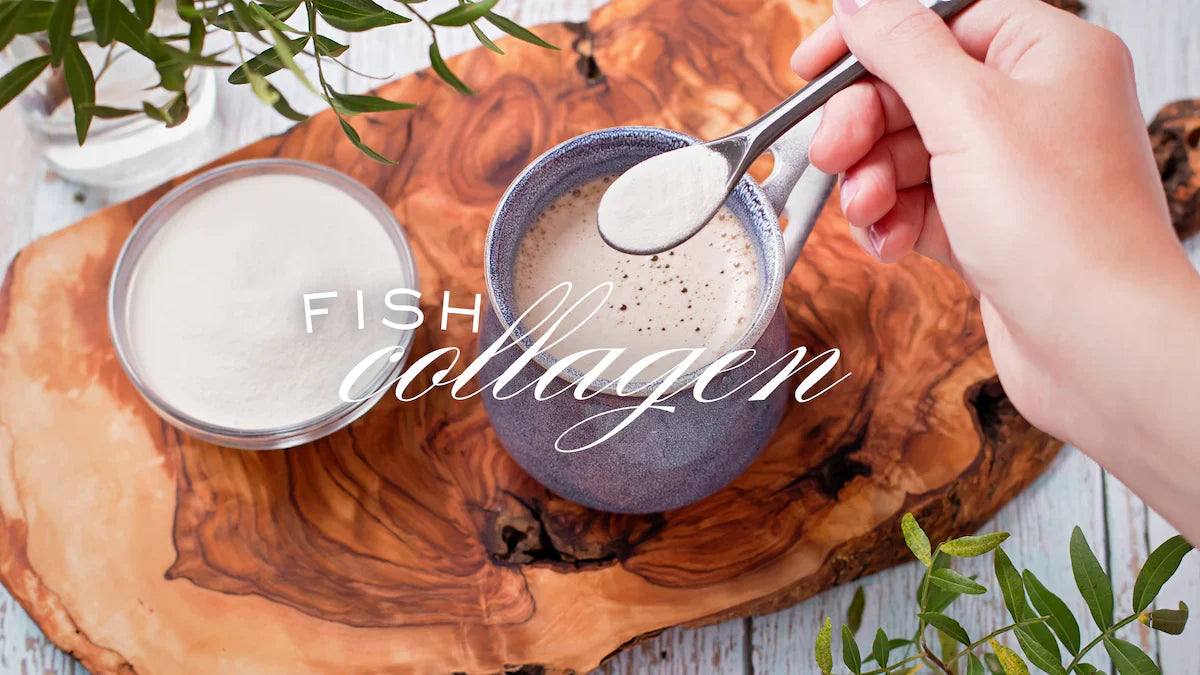 Eine Hand löffelt pulverförmiges Fischkollagen in eine Tasse Getränk auf einem rustikalen Holzbrett, daneben eine Schale mit Kollagenpulver.
