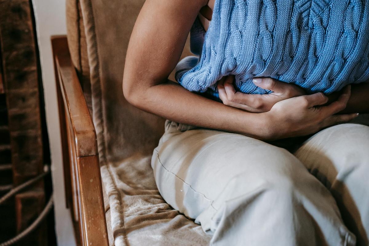 Person sitzt auf einem Sessel und hält sich mit beiden Armen den Bauch, während sie ein blaues Wärmekissen gegen den Unterleib drückt – Symbolbild für Bauchschmerzen oder entzündliche Darmbeschwerden.