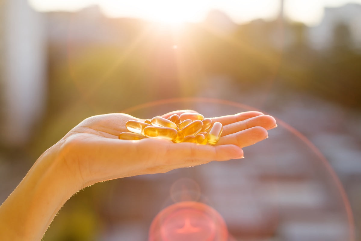 Hand einer Frau, die eine Handvoll Omega-3-Fischölkapseln im Sonnenlicht hält.