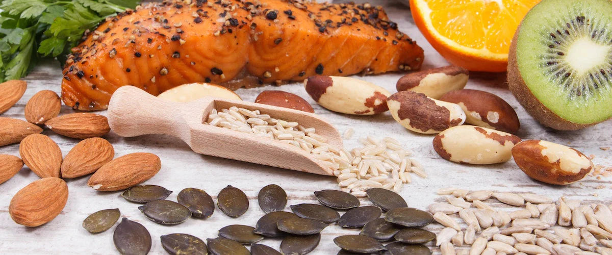 Nahaufnahme verschiedener nährstoffreicher Lebensmittel, darunter gebratener Lachs, Kiwi, Orange, Mandeln, Paranüsse, Kürbiskerne und Sonnenblumenkerne.