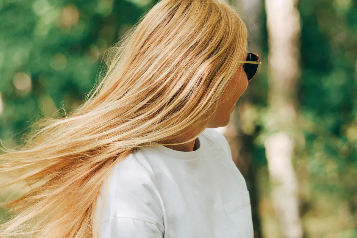 Frau mit langen, blonden Haaren in der Natur – Symbol für gepflegtes Haar und natürliche Vitalität.
