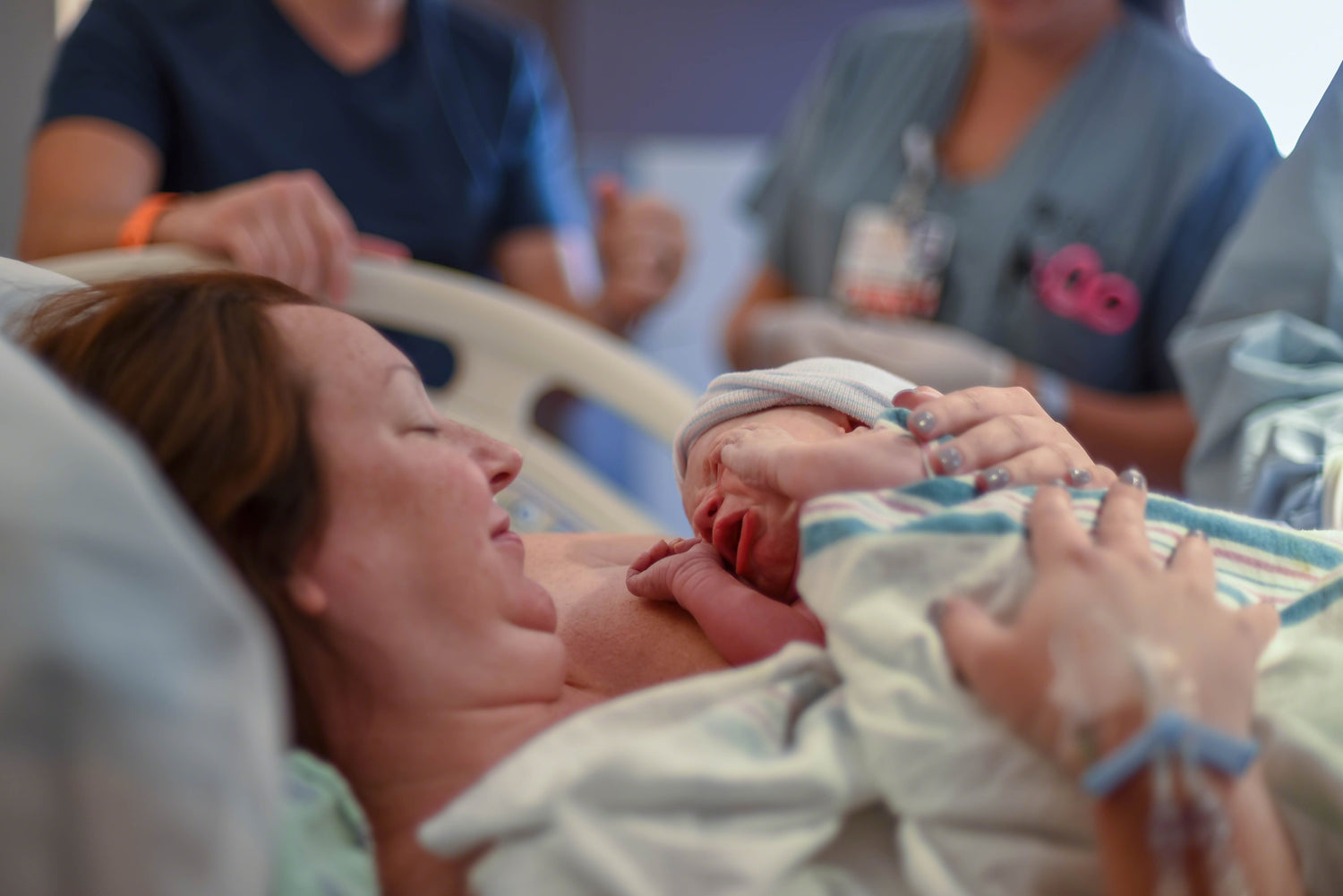 Mutter hält ihr neugeborenes Baby direkt nach der Geburt im Krankenhaus, umgeben von medizinischem Personal.