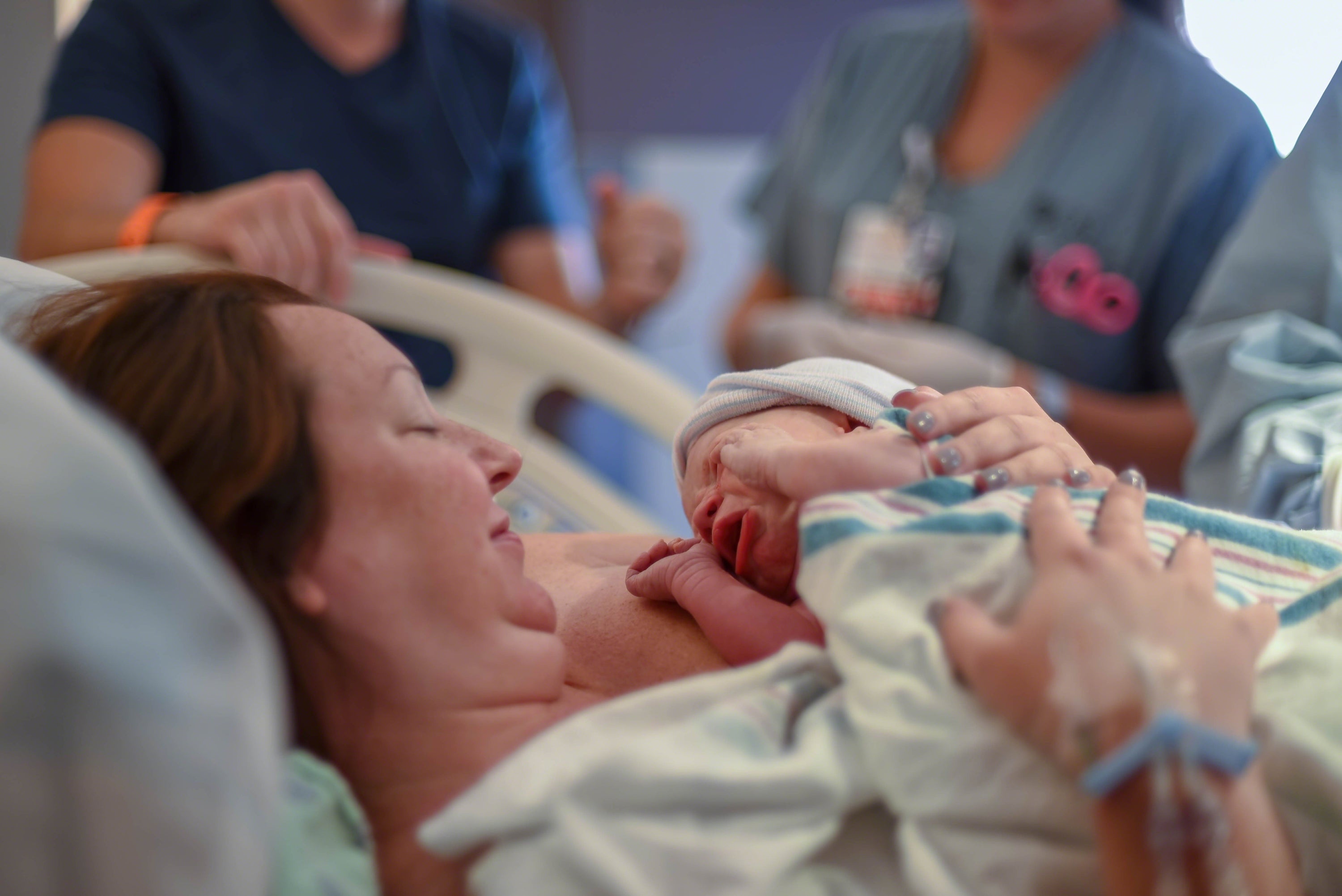 Mutter hält ihr neugeborenes Baby direkt nach der Geburt im Krankenhaus, umgeben von medizinischem Personal.