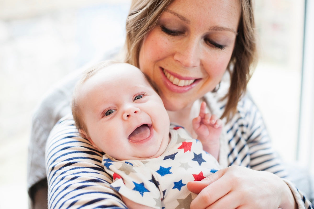 Lächelnde Mutter hält fröhliches Baby im Arm, beide in gestreifter Kleidung – inniger Moment voller Nähe und Geborgenheit.