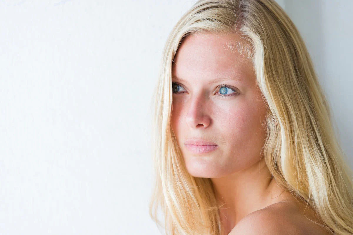 Porträt einer jungen blonden Frau mit klarer, glatter Haut, die nachdenklich seitlich in die Ferne blickt – Symbol für natürliche Schönheit und gesunde Hautpflege.
