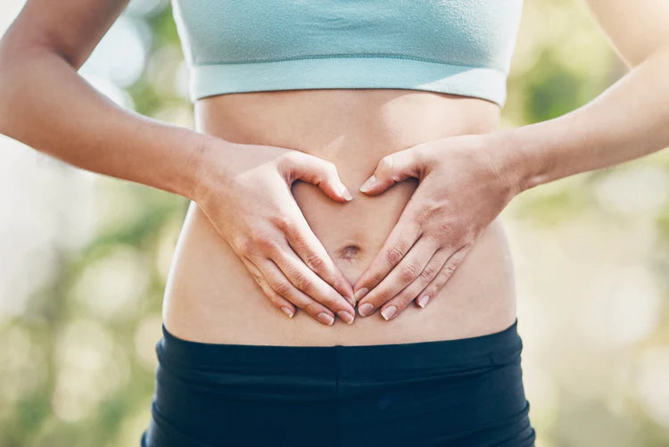 Nahaufnahme des Bauches einer jungen Frau in Sportkleidung, die mit ihren Händen eine Herzform über dem Bauch macht.